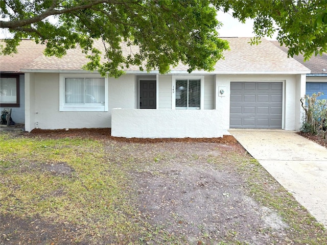 ranch-style house with a shingled roof, concrete driveway, and stucco siding