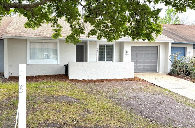 ranch-style home featuring an attached garage, a shingled roof, concrete driveway, and stucco siding