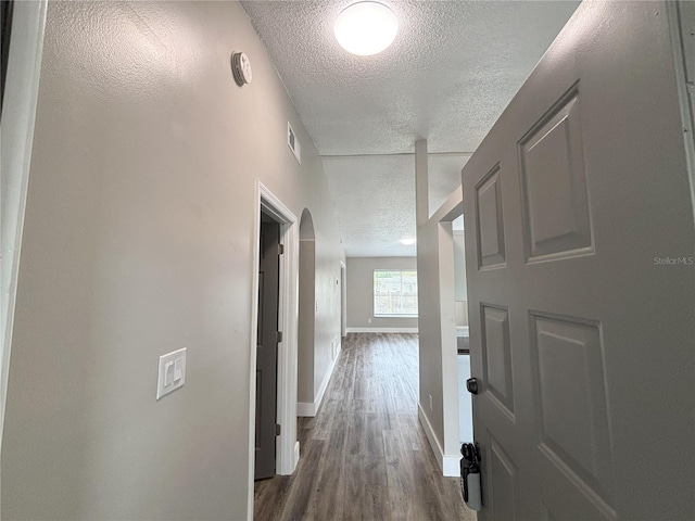 hallway featuring visible vents, baseboards, dark wood finished floors, and a textured ceiling