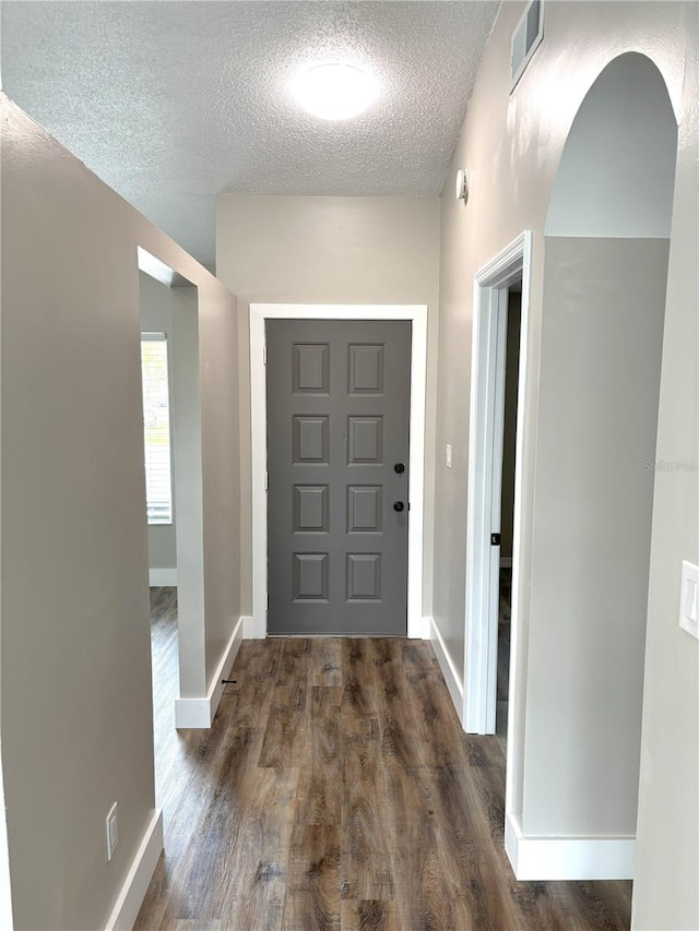 entryway featuring arched walkways, visible vents, dark wood-type flooring, a textured ceiling, and baseboards