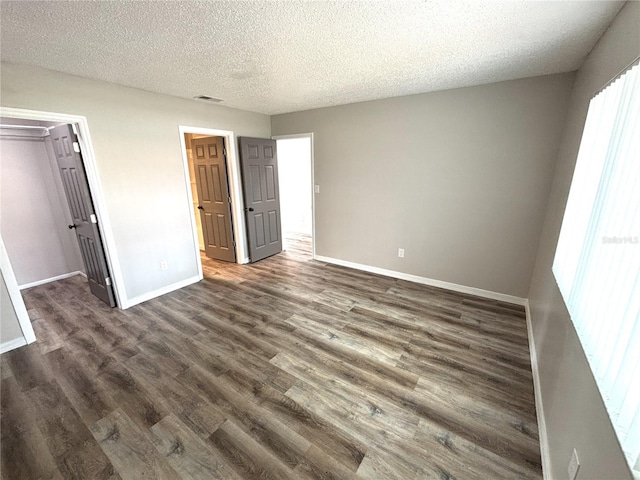 unfurnished bedroom featuring a textured ceiling, dark wood-style flooring, visible vents, baseboards, and a spacious closet