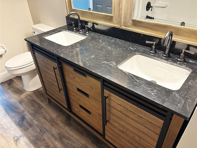 full bath with double vanity, a sink, toilet, and wood finished floors