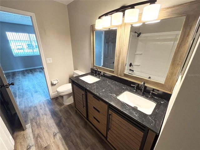 bathroom featuring toilet, double vanity, a sink, and wood finished floors