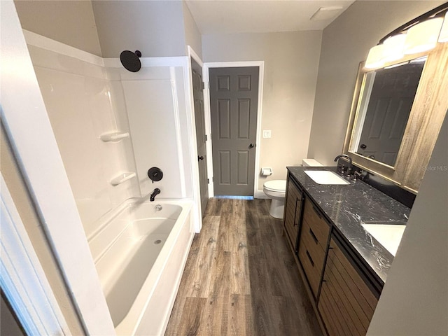 bathroom with double vanity, shower / bathtub combination, toilet, a sink, and wood finished floors