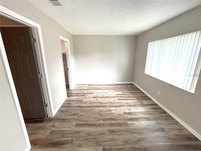 empty room featuring baseboards, a textured ceiling, visible vents, and dark wood-type flooring