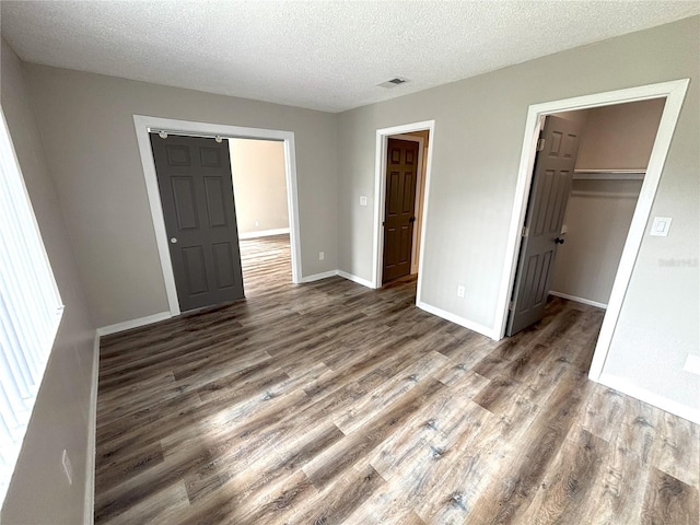 unfurnished bedroom featuring dark wood-type flooring, a spacious closet, baseboards, and a textured ceiling