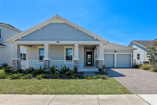 craftsman-style house featuring stucco siding, decorative driveway, stone siding, covered porch, and a garage