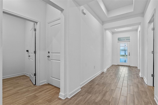 hallway featuring light wood finished floors, a tray ceiling, and baseboards