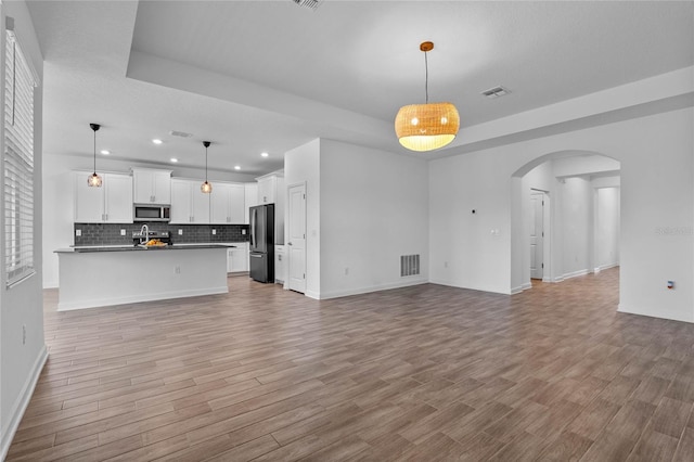 unfurnished living room featuring a tray ceiling, visible vents, arched walkways, and light wood finished floors