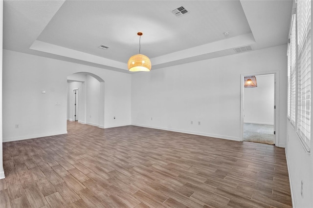 empty room featuring a tray ceiling, arched walkways, visible vents, and wood finished floors