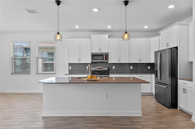 kitchen with visible vents, a sink, stainless steel appliances, tasteful backsplash, and light wood-type flooring