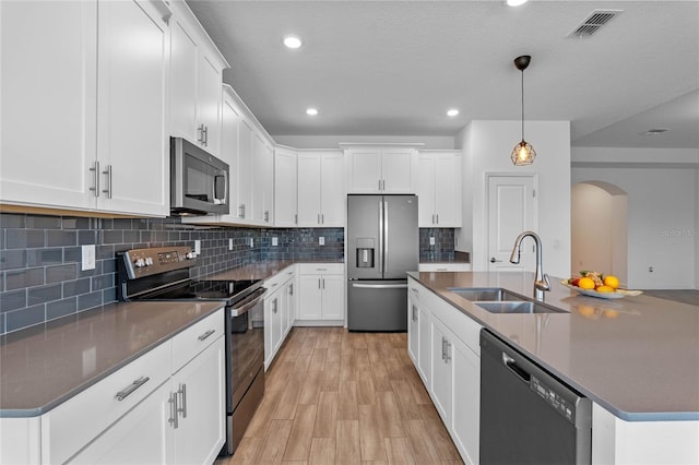 kitchen with a kitchen island with sink, a sink, dark countertops, stainless steel appliances, and arched walkways