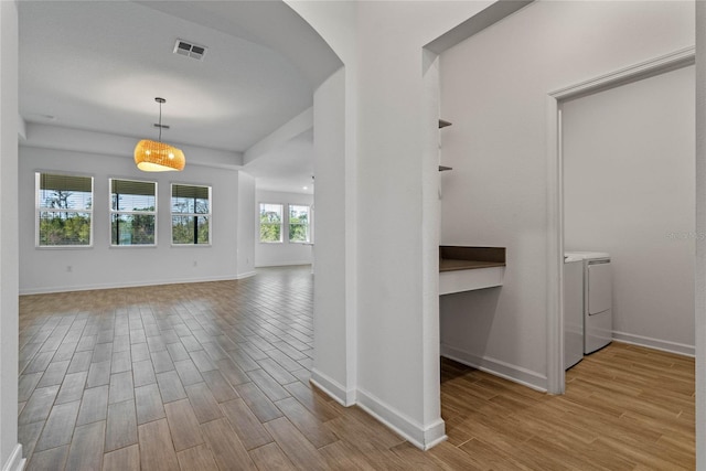 corridor with washer and dryer, wood finished floors, arched walkways, and baseboards