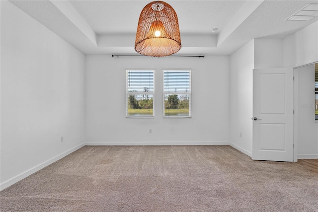 carpeted empty room featuring baseboards, a raised ceiling, a notable chandelier, and visible vents