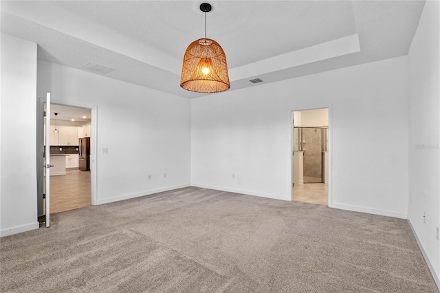 carpeted empty room featuring visible vents, a raised ceiling, and baseboards