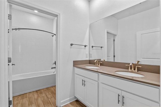 bathroom with double vanity, washtub / shower combination, wood finished floors, and a sink