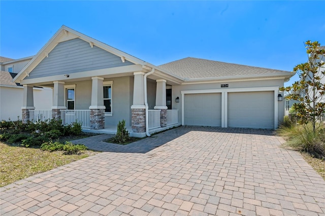 view of front of home featuring stucco siding, decorative driveway, stone siding, covered porch, and an attached garage