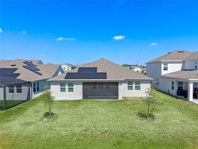 back of house featuring stucco siding, roof mounted solar panels, a yard, roof with shingles, and a sunroom