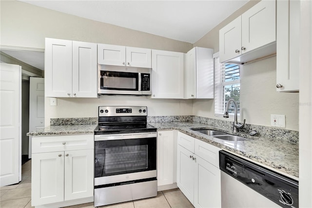 kitchen featuring light tile patterned floors, stainless steel appliances, white cabinetry, a sink, and light stone countertops