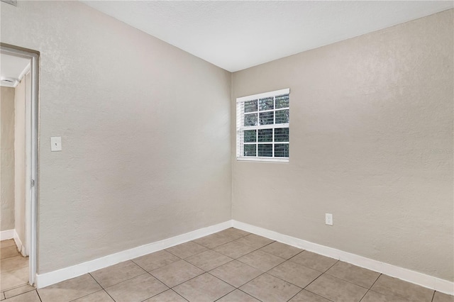 unfurnished room featuring light tile patterned flooring, baseboards, and a textured wall