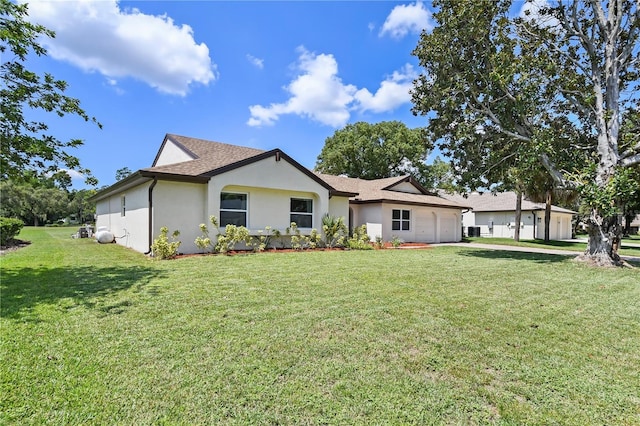 rear view of house with an attached garage, roof with shingles, a lawn, and stucco siding