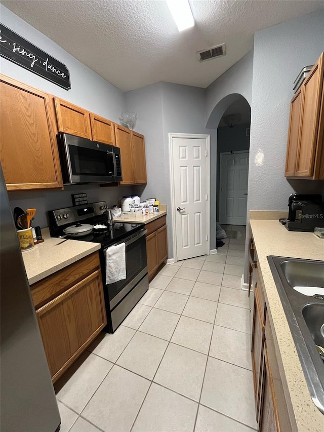 kitchen with visible vents, stainless steel electric stove, light tile patterned floors, arched walkways, and a sink