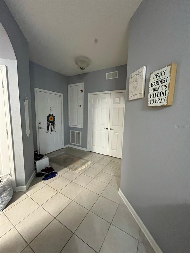 hall featuring visible vents, arched walkways, baseboards, and light tile patterned flooring