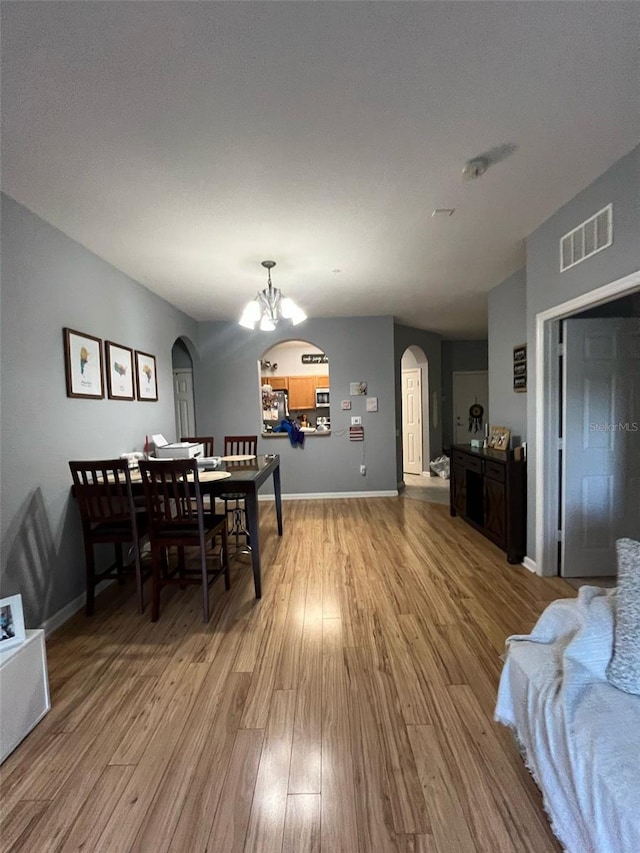 dining area with visible vents, a notable chandelier, arched walkways, light wood-style floors, and baseboards