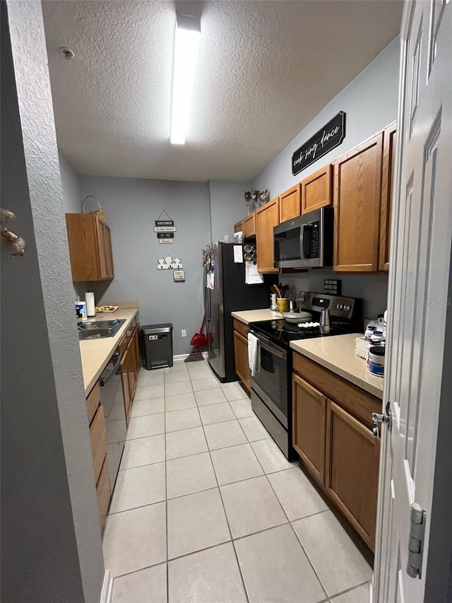 kitchen with a sink, a textured ceiling, appliances with stainless steel finishes, light tile patterned flooring, and light countertops