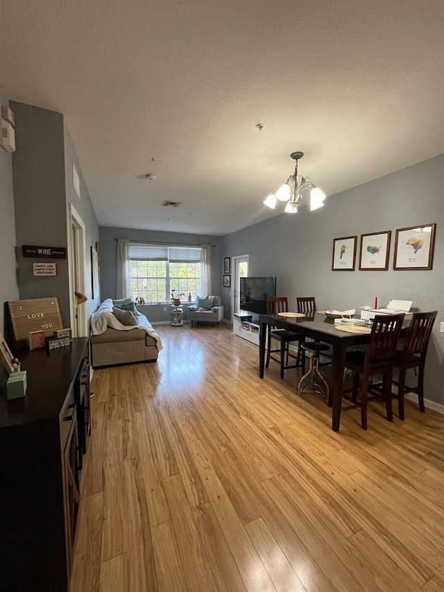 dining area featuring visible vents, light wood-style flooring, a textured ceiling, an inviting chandelier, and baseboards