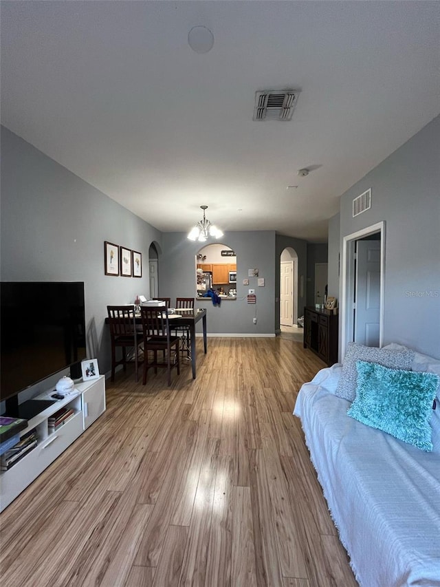 living area featuring wood finished floors, a notable chandelier, visible vents, and arched walkways