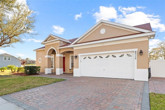 view of front facade featuring a garage, decorative driveway, fence, and stucco siding