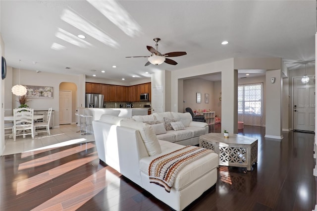 living area featuring arched walkways, recessed lighting, light wood-style floors, a ceiling fan, and baseboards