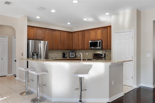 kitchen featuring arched walkways, decorative backsplash, an island with sink, appliances with stainless steel finishes, and a breakfast bar