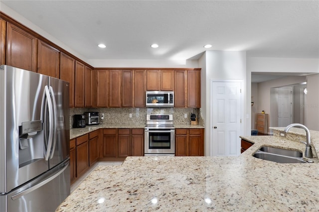 kitchen featuring light stone counters, brown cabinets, decorative backsplash, appliances with stainless steel finishes, and a sink