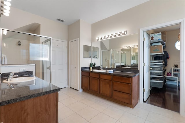 full bath featuring a stall shower, visible vents, tile patterned floors, a sink, and two vanities