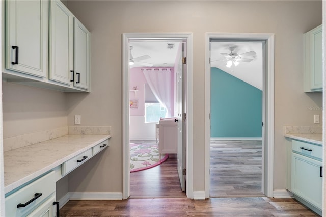 kitchen featuring light stone counters, a ceiling fan, baseboards, and wood finished floors