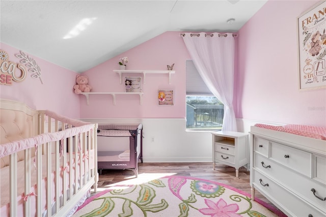 bedroom with lofted ceiling, a crib, and light wood-type flooring