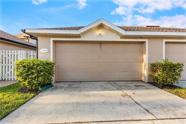 view of front of property featuring a garage, driveway, fence, and stucco siding