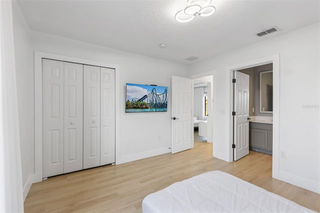 bedroom with baseboards, visible vents, ensuite bath, a textured ceiling, and light wood-type flooring