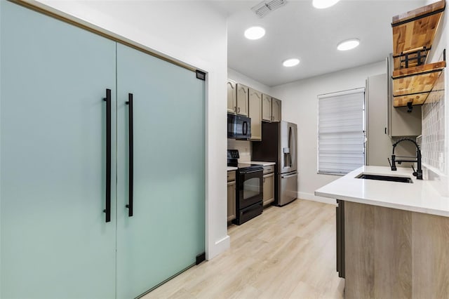 kitchen featuring a sink, visible vents, light wood-style floors, light countertops, and black appliances