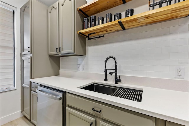 kitchen with a sink, light countertops, stainless steel dishwasher, gray cabinets, and decorative backsplash