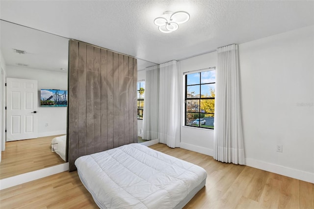 bedroom featuring light wood-type flooring, baseboards, visible vents, and a textured ceiling