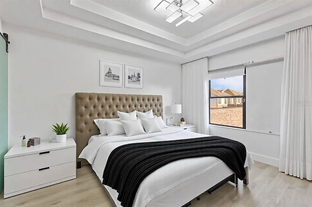 bedroom with a tray ceiling, a barn door, and light wood-style floors