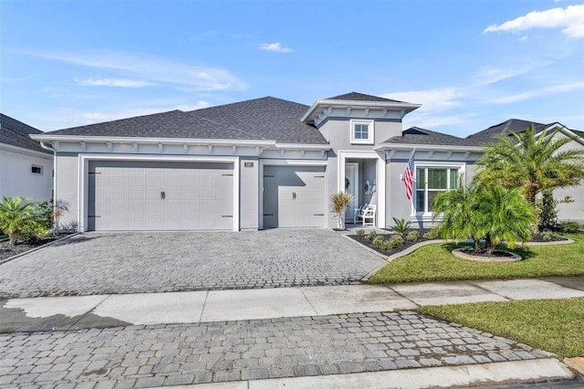 prairie-style house featuring a front yard, decorative driveway, an attached garage, and stucco siding