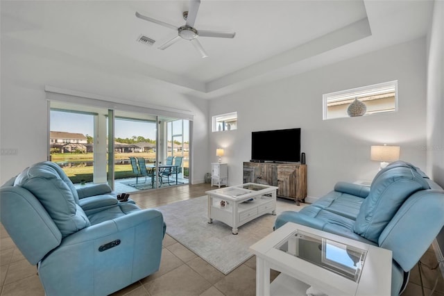 living room featuring ceiling fan, light tile patterned floors, visible vents, baseboards, and a tray ceiling