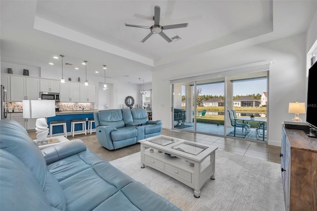 living room featuring baseboards, visible vents, a ceiling fan, a tray ceiling, and light tile patterned flooring