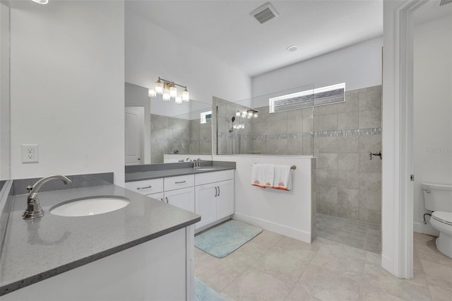 bathroom with a walk in shower, toilet, two vanities, visible vents, and a sink