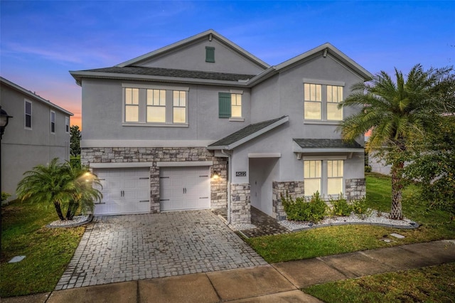 traditional-style house with stone siding, decorative driveway, an attached garage, and stucco siding