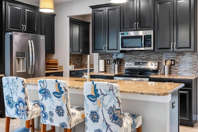 kitchen featuring stainless steel appliances, dark cabinetry, decorative backsplash, and light stone counters